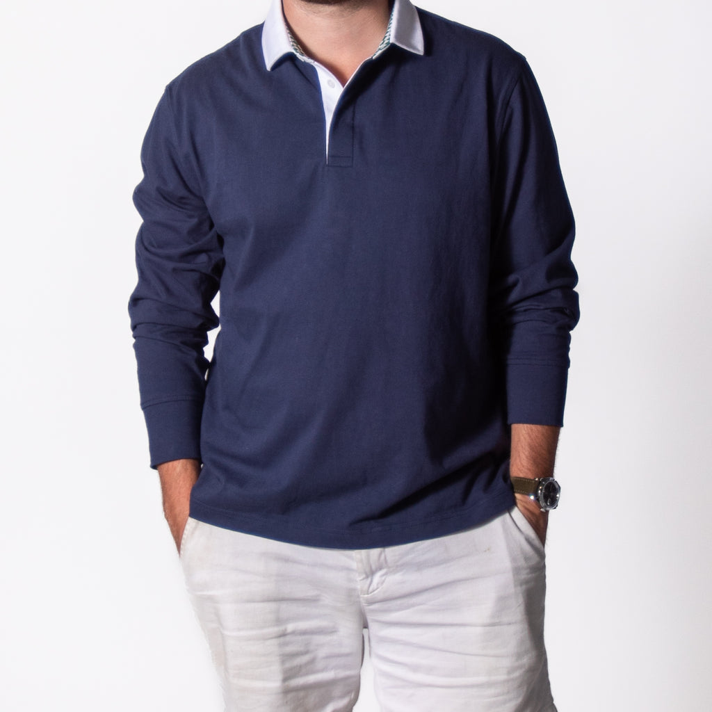 Man wearing a navy rugby shirt with light-colored pants on a white background