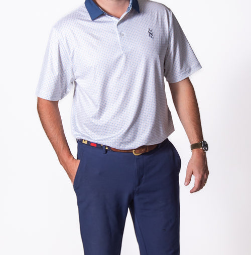 Person wearing a white polo shirt with a small logo and navy pants on a white background