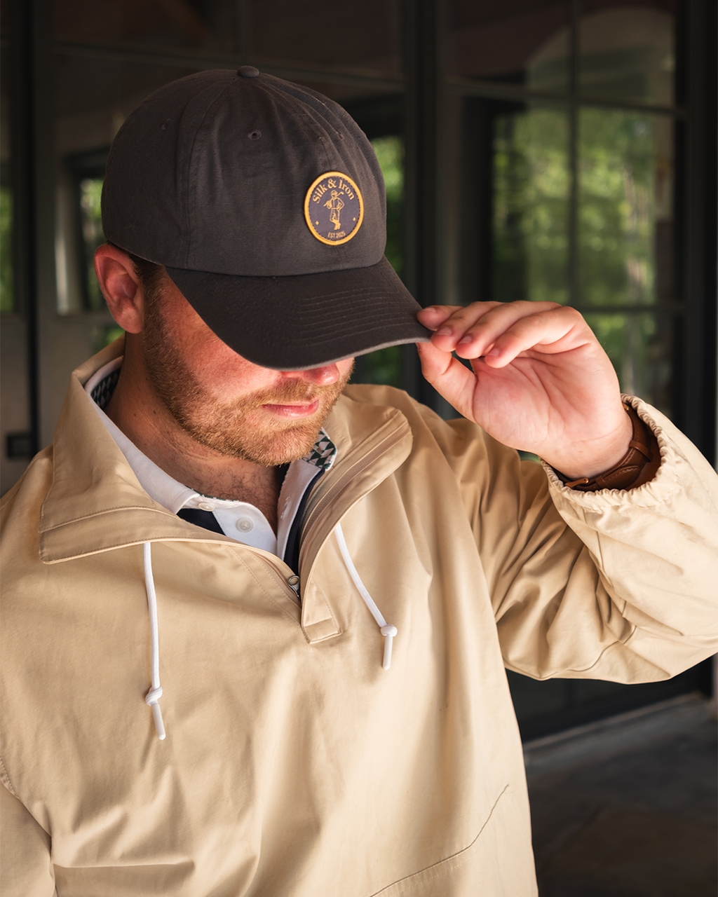 Man wearing a beige jacket and dark cap with a logo, adjusting the cap.